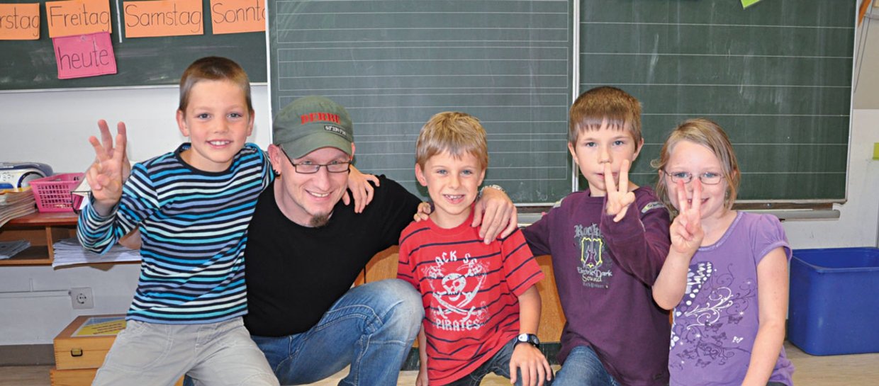 Vier Kinder und ein Mann sind in einem Klassenzimmer lächeln in die Kamera.